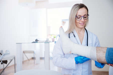 Smiling proffesional nurse in glasses bandages the leg.の写真素材