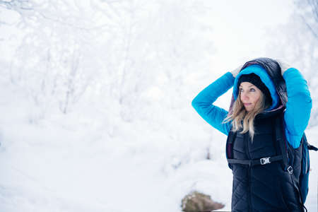 A blonde tourist in a blue jacket on a mountain trail in winter.の写真素材