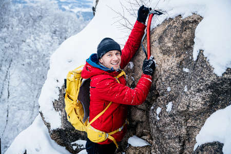 Handsome smiling mountaineer with an ice ax while climbing the rocks.の写真素材