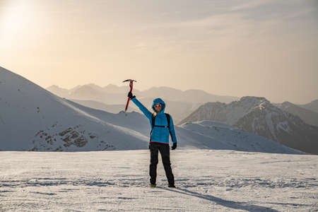 A female climber with an ice ax raised in her hand on a beautiful winter day.