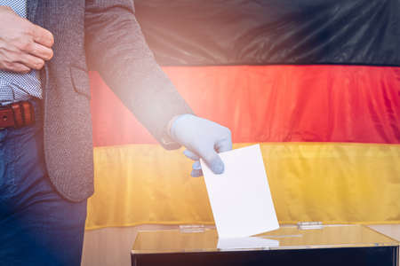Person in a jacket wearing blue protective latex rubber gloves putting ballot paper in vote box.