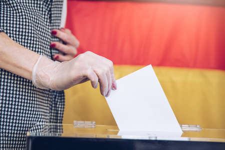 Voting on elections during pandemic. A womans hand in gloveputs her vote into the ballot box.の写真素材