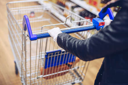 Close up of woman hands in protective gloves pushing shopping cart in supermarket.の写真素材
