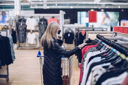 Woman wearing medical mask and gloves shopping in clothes department during COVID.