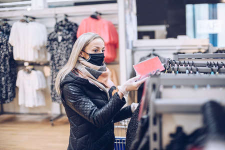 Blonde woman wearing a face mask while shopping in a clothing department store or supermarket.の写真素材