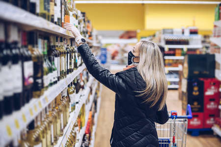 Woman wearing medical mask is choosing wine in the supermarket.の写真素材