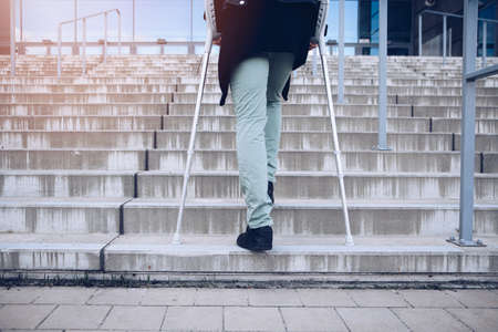 Man on crutches climbs a big set of stairs.の写真素材