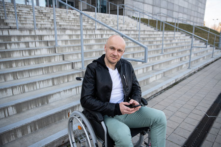 Man at black jacket in a wheelchair with phone in hand.の写真素材