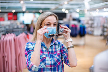Woman chooses sunglasses in supermarket during pandemic.の写真素材
