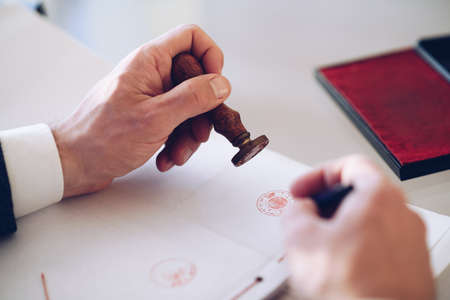 Close-up of a persons hand stamping with approved stamp on certificate or other document.