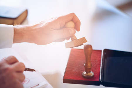 Close-up of a persons hand stamping with approved stamp on certificate document public paper.の写真素材