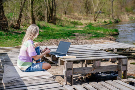 A blonde woman works remotely in beautiful sunny weather. Woman working outdoors.の写真素材