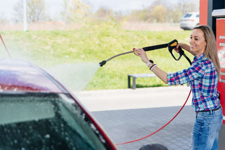 Beauty woman at the self-service car wash station washing the foam off her car.の写真素材
