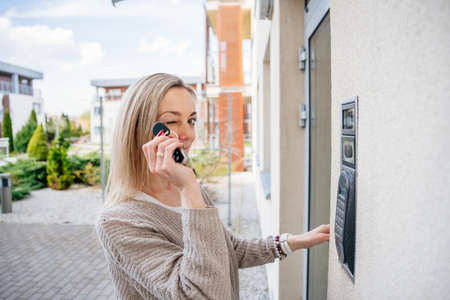 The blonde woman winks while holding the remote control to enter the house.