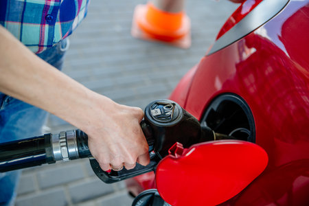 Womans hand manually filling a car with gasoline, fuel at a refueling station.