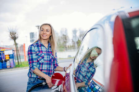 Pretty blonde fills her red car with gasoline at the gas stationの写真素材