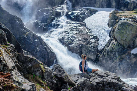 A happy traveler admires a beautiful waterfall on a sunny day.の写真素材