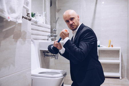 A man holding a plunger to clear a plugged toilet.の写真素材