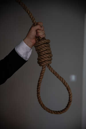 A businessmans hand is holding a noose of rope to hang.