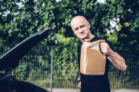 Handsome man in black t-shirt holding bottle with engine oil.