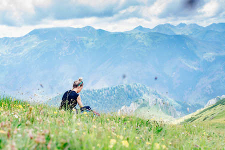 Back view of a blond female traveler resting on the grass during a mountain trek.の写真素材