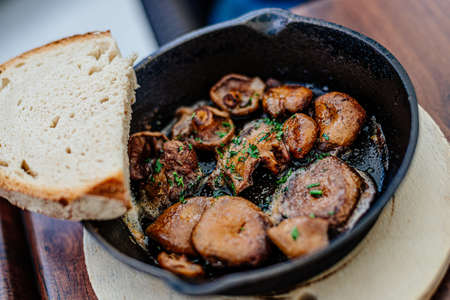 Frying pan of mushrooms and slice of bread on wooden plank.の写真素材
