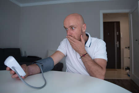A scared man with high blood pressure measures the pressure in his home in the morning.の写真素材