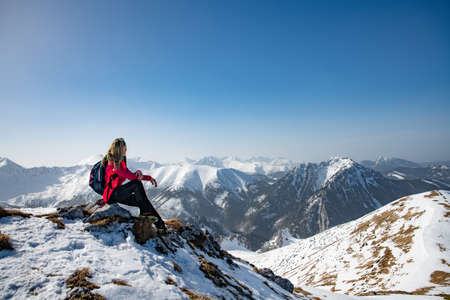 Blonde female tourist sit on the rock. Winter hiking scene.の写真素材