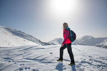 Female tourist in a red jacket goes mountain trail in beautifull winter day.の写真素材