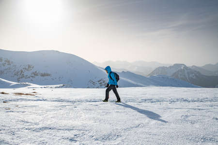 Female tourist in a blue jacket goes mountain trail in beautifull winter day.の写真素材