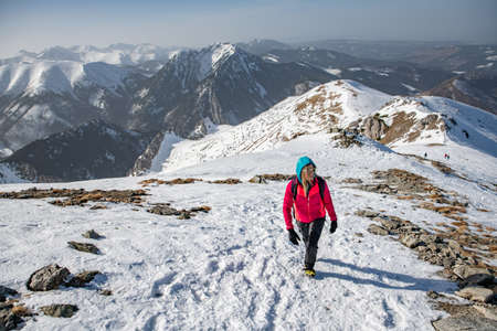 Blonde woman in the red jacket and black pants with sunglasses is goes beautiful mountain trail.の写真素材
