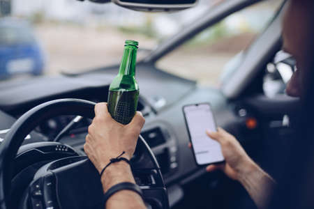 Drunk driver drinking alcohol in car and using phoneの写真素材