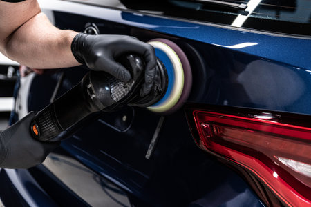 Employee of a car detailing studio polishes the paint of a carの写真素材