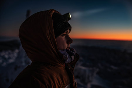 Teenager boy in a warm winter jacket with a headlamp on a mountain winter trail.の写真素材