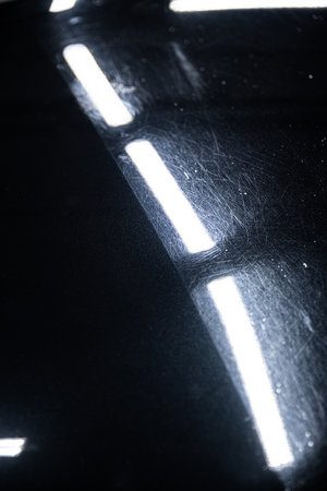 Before and after effect of a paint correction on the paintwork of a black car in a car detailing...