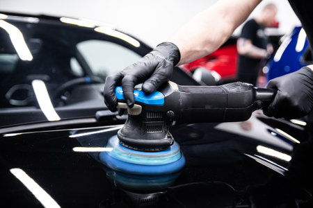 Mechanic wearing black gloves polishing car paint with a machine in a detailing studio.の写真素材