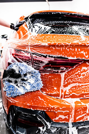Car wash or detailing employee thoroughly cleans an orange carの写真素材