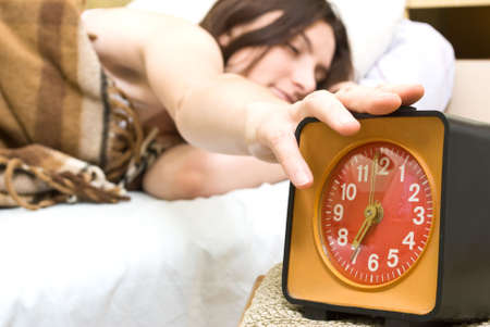 Young woman snoozing a red alarm clockの写真素材