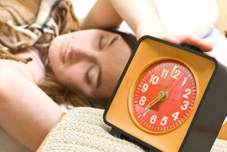 Young woman snoozing a red alarm clockの写真素材