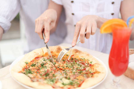 Cutting a  pizza with knife in cafeの写真素材
