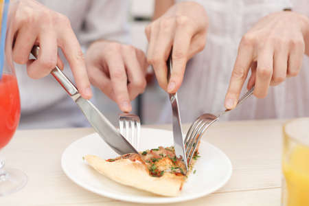 Hands  cutting  a slice of a pizza in cafeの写真素材