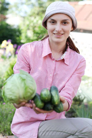 Happy girl with cabbage and cucumbers in gardenの写真素材