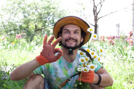 Funny  man holding the camomile bouquet and the sickle in the gardenの写真素材