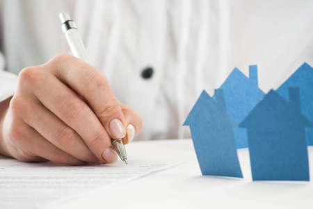 Hand filling out the form with paper houses in foreground.の写真素材