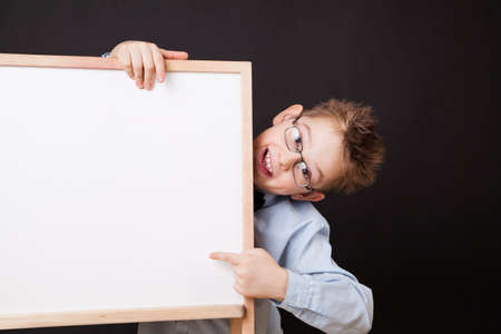 Portrait of cheerful boy pointing on white banner on the black backgroundの写真素材