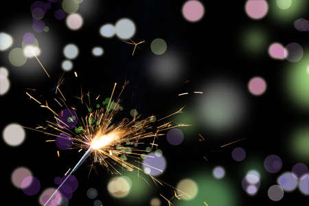 Lighted Christmas sparkler on colorful lights background.