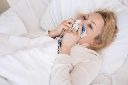 Sick woman lying in bed with high fever. Cold flu and migraineの写真素材