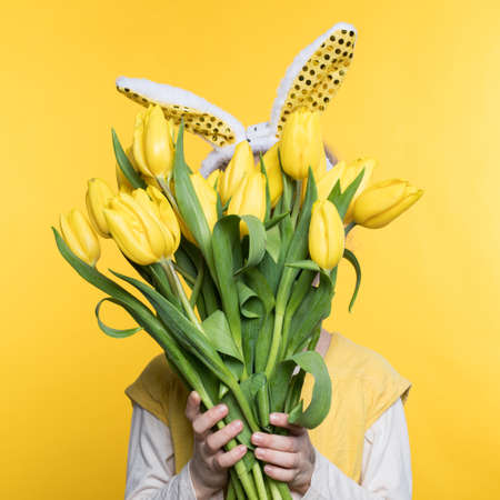 Smiling little girl with bunny ears with flowers on a yellow backgroundの写真素材