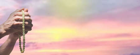 praying beads in hands over the sky backgroundの写真素材