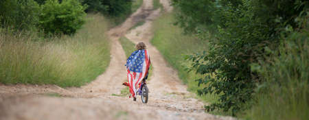 Symbol of celebration 4 fourth of july. Young Girl riding bicycle with american flag in handの写真素材